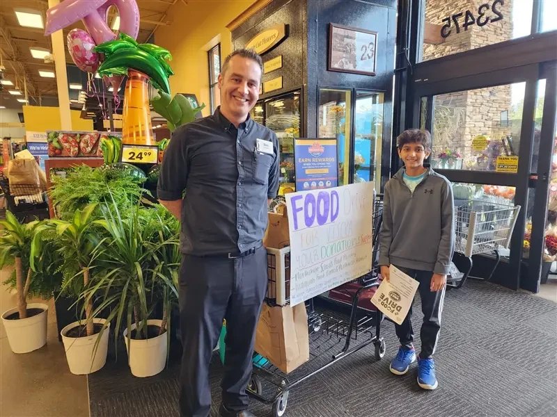 Smaran next to a food drive cart and sign at a grocery store