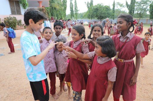Smaran playing a hand game with students in school uniforms